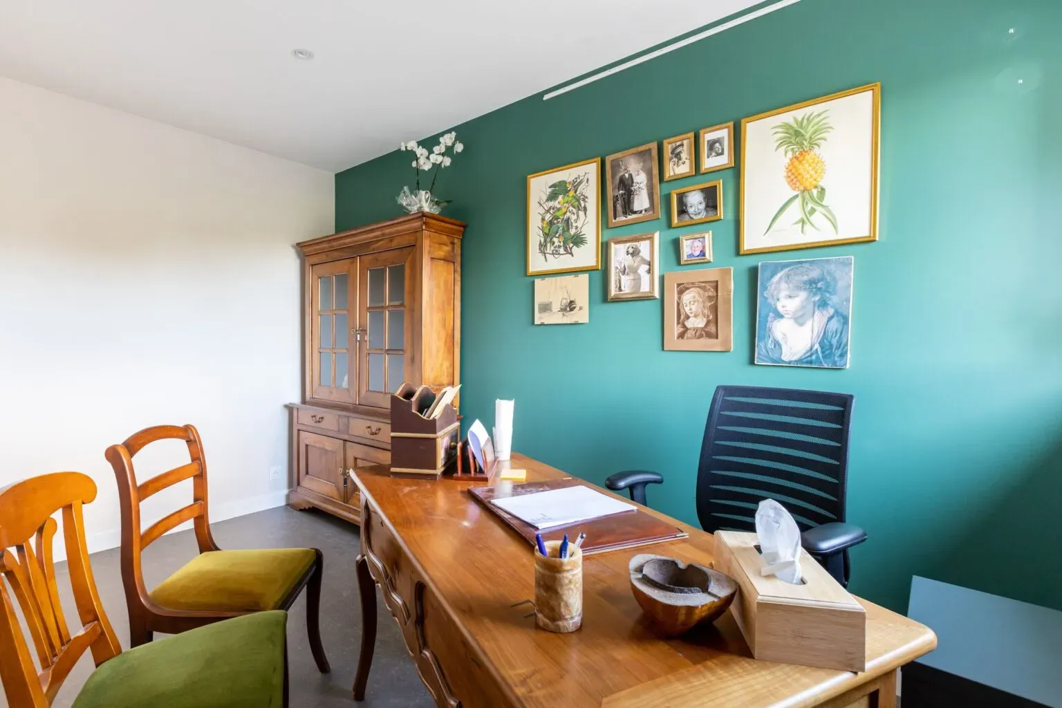 Bureau d'accueil en bois, mur vert avec cadres photos variés.