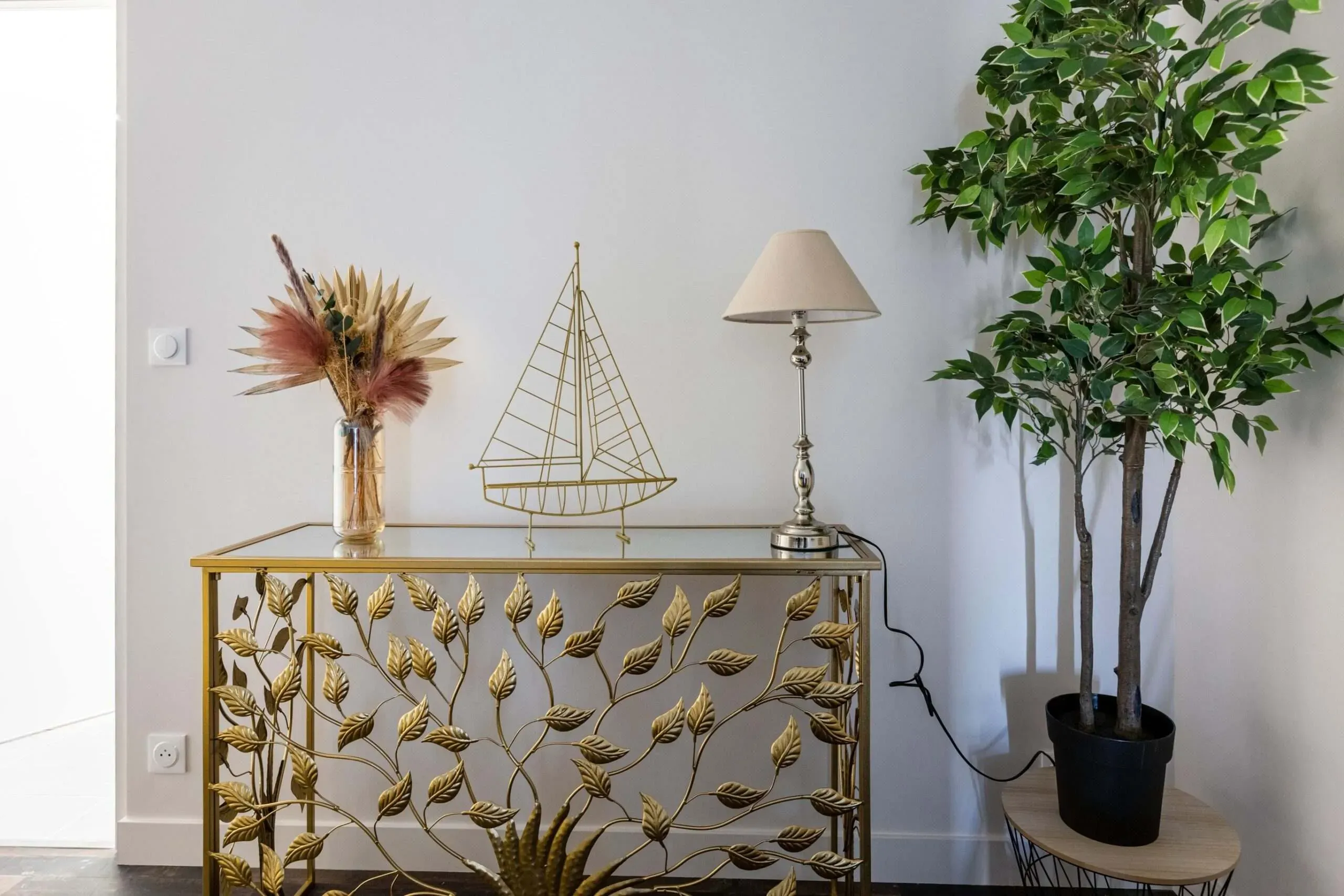 Console dorée design avec bouquet fleurs séchées, voilier et lampe.